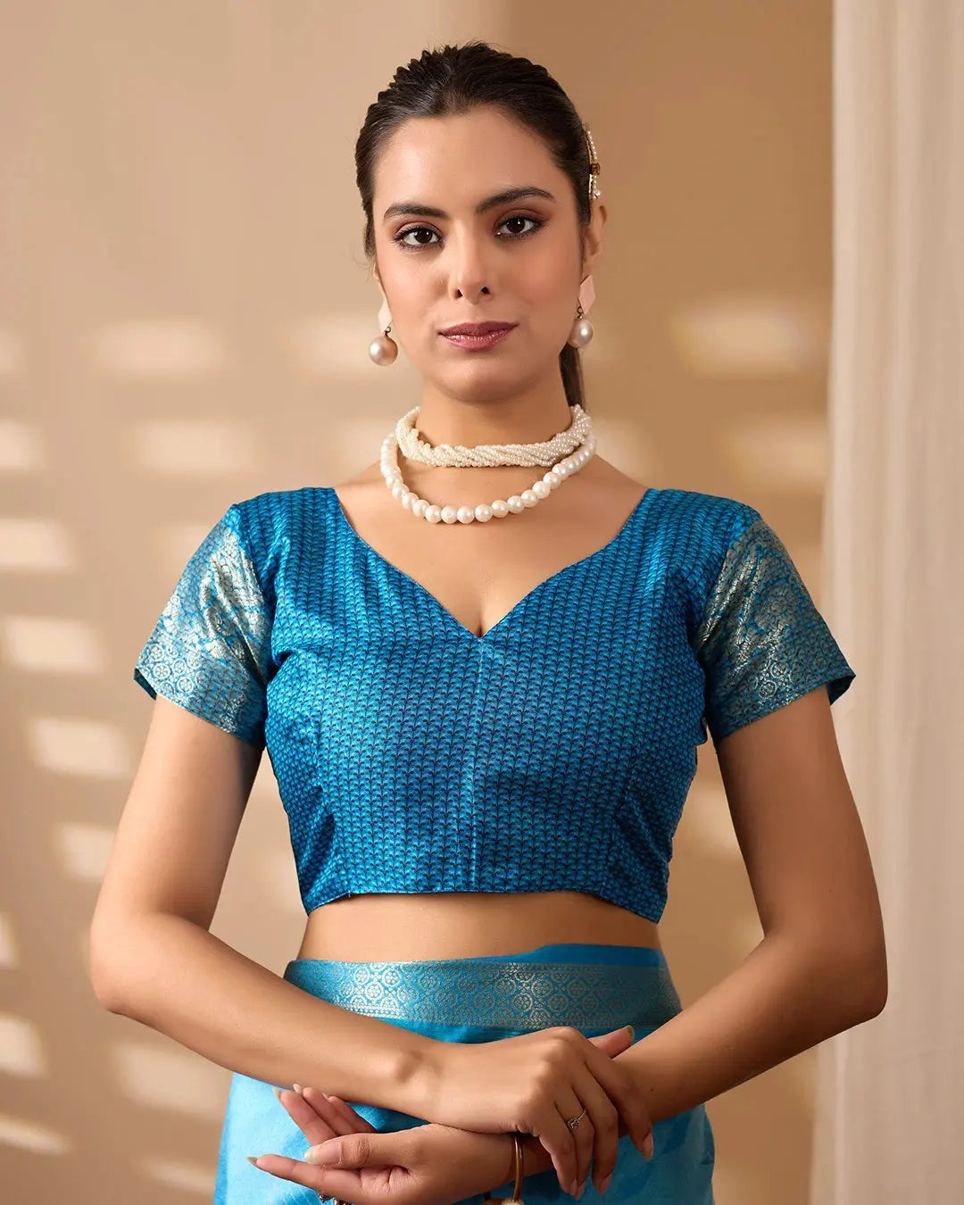 Woman wearing a blue traditional outfit with a pearl necklace against a beige background